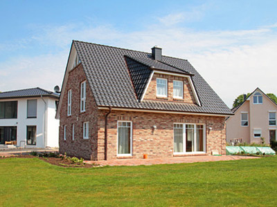 Ein modernes, zweigeschossiges Haus mit Ziegelfassade und Satteldach, umgeben von einer grünen Wiese.